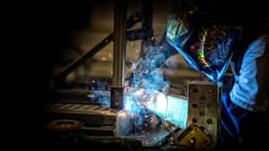 A Welder Is Welding Metal In A Dark Room Wallpaper