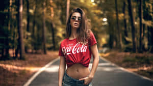 A Woman In A Red Coca Cola Shirt Standing On A Road Wallpaper