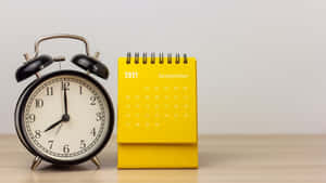 A Yellow Alarm Clock Next To A Calendar Wallpaper