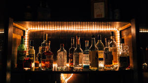 Alcohol Bottles On Shelf With Light Wallpaper