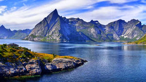 Angular Rocky Mountains Over Huge Body Of Water Wallpaper