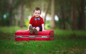 Baby Boy Seated On Red Suitcase Wallpaper