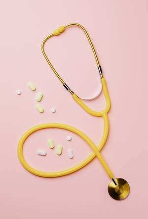 Caption: A Bright Yellow Stethoscope With Medicine Books - Symbolizing Mbbs Studies Wallpaper
