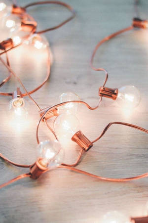 Caption: Elegance Illuminated - Rose Gold Light Bulbs Wallpaper