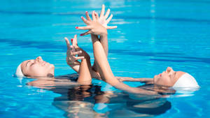 Caption: Harmonious Gestures In Artistic Swimming Wallpaper