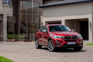 Caption: Luxurious Bmw X6 M Parked Outside A Modern House Wallpaper