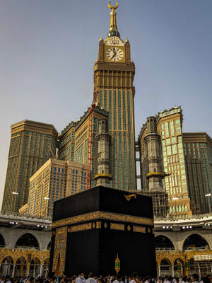 Caption: Majestic View Of The Clock Tower And Kaabah In Makkah Madina Wallpaper