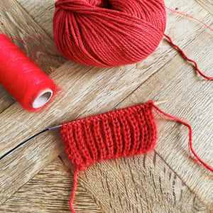 Caption: Passionate Hands Knitting A Red Cotton Yarn Wallpaper