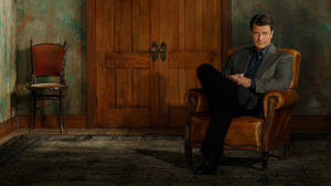 Casual Pose Of Actor Nathan Fillion Lounging On A Chair Wallpaper