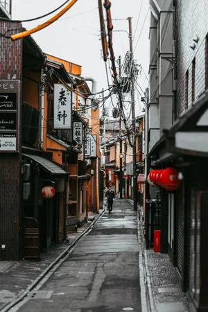 Charming Exploration - A Solitary Wanderer Traverses A Narrow Street In Japan. Wallpaper