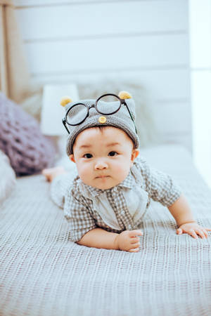 Cute Baby On Bed With Eyeglasses Wallpaper
