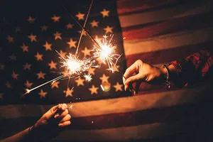 Dark American Flag Behind Two Hands Holding Sparklers Wallpaper