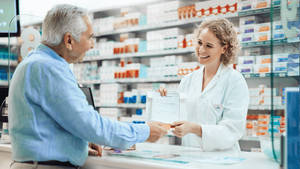Dedicated Pharmacist Assisting Senior Patient Wallpaper