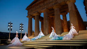 Dolce And Gabbana Models Sitting Beneath Pillars Wallpaper