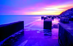 Enjoy The Beauty Of Nature As The Sun Dips Over The Horizon Casting A Beautiful Blue And Purple Sunset. Wallpaper
