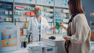 Experienced Female Pharmacist Assisting A Customer Wallpaper