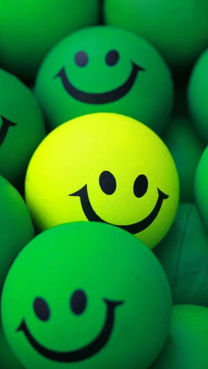 Expressive Yellow Smiley Ball Amongst Green Balls Wallpaper