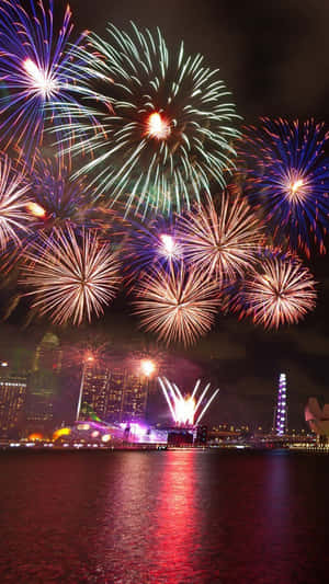 Fireworks Over The Water With A City In The Background Wallpaper