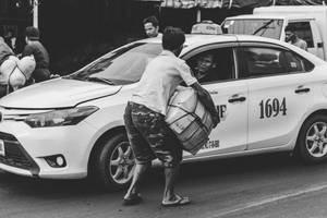 Greyscale Photography Of Man Carrying Cardboard Box Beside Taxi Wallpaper