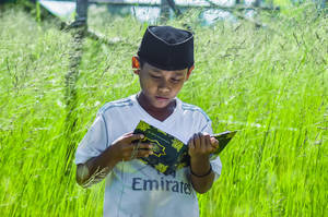 Islamic Boy Reading Quran Outdoors Wallpaper