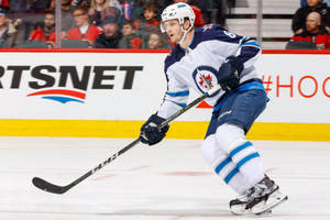 Jacob Trouba Holding Hockey Stick While Leaning To The Right With Mouth Open Wallpaper