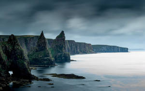 Jagged Cliffs And Calm Sea Background Wallpaper