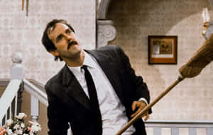 John Cleese With Broom Comedic Scene Wallpaper