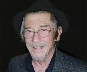 Legendary Actor John Hurt In Hat And Glasses Against A Black Background Wallpaper