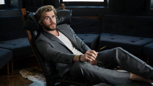 Liam Hemsworth Sitting On Black Couch Wallpaper