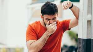 Man Feeling Nauseous In Orange Shirt Against A Natural Backdrop Wallpaper