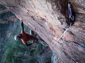 Man Rock Climbing On A Flip Rock Structure Wallpaper