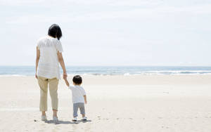 Mother And Son Walk Hand In Hand On The Beach Wallpaper