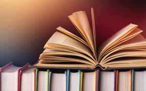 Opened Book Laying On Top Of A Stack Of Multicolored Books Wallpaper