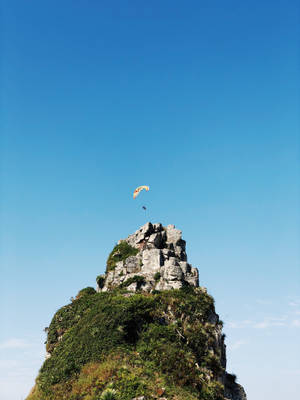 Paragliding Above Pointed Rock Cliff Wallpaper