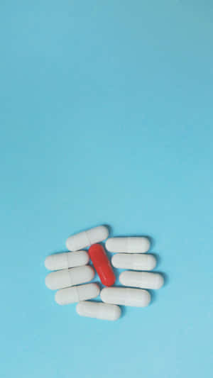 Red Pill Among White Capsuleson Blue Background Wallpaper