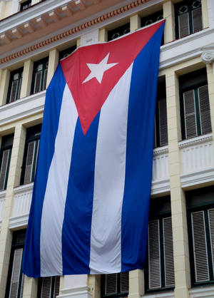 The Authentic Cuban Flag Waving In Front Of A Classical Cuban Building. Wallpaper