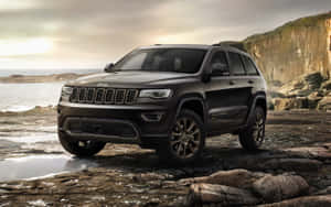 The New Jeep Grand Cherokee Is Parked On A Rocky Beach Wallpaper