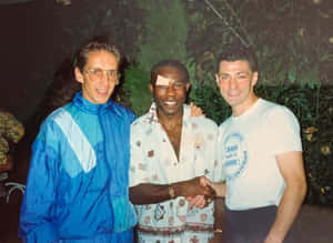 Three Men Shaking Hands Outdoors Wallpaper