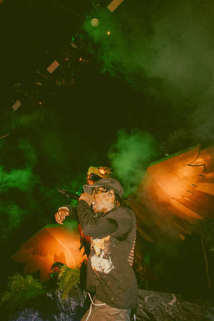 Travis Scott Delivering An Energetic Performance Illuminated By Yellow And Orange Flames Wallpaper