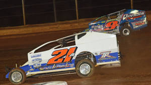 Two Dirt Cars Racing On A Dirt Track Wallpaper