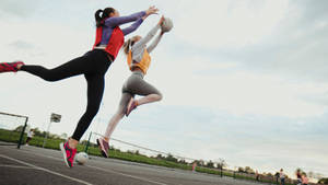 Two Girls Jump Race Catching Ball Netball Wallpaper