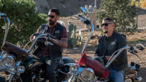 Two Men On Motorcycles Sitting On Dirt Wallpaper