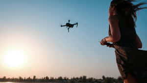 Woman Controlling Droneat Sunset Wallpaper