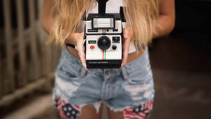Young Girl Capturing Memories With Classic Polaroid Camera Wallpaper